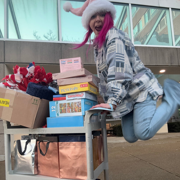 Person with pink hair and a white hat standing next to a display of bags and boxes outside a store.